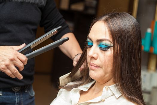 Stylist Using Flat Iron on Hair of Female Client Sitting in Salon Chair