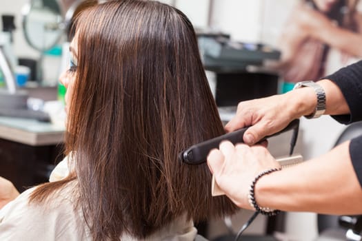 Stylist Using Flat Iron on Hair of Female Client Sitting in Salon Chair