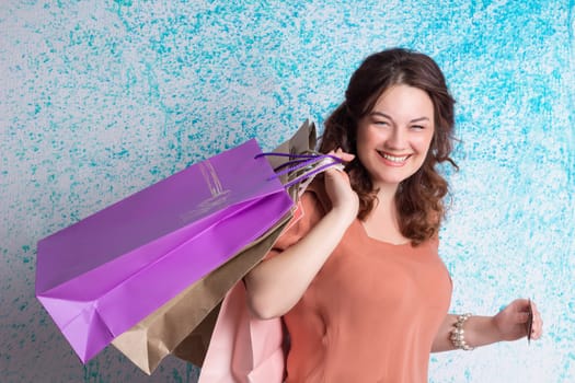 Happy smiling woman in orange blouse holding colourful shopping paper bags