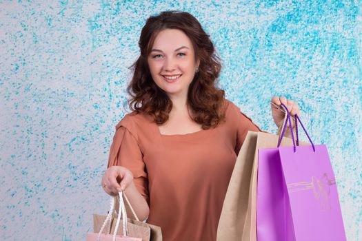 Happy smiling woman in orange blouse holding colourful shopping paper bags