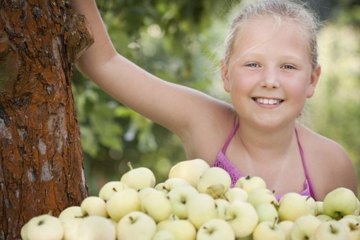 Nice young girl with stack of green fresh apples in the orchard