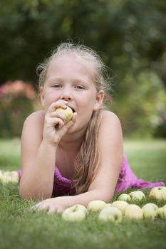 Nice young girl with stack of green fresh apples in the orchard