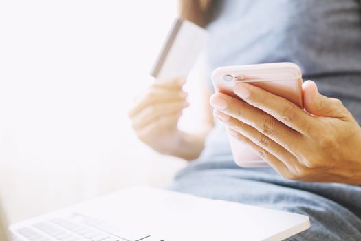 female hands holding credit card and using phone and computer laptop. Online shopping purchase Sell or Payment.