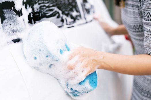Female hand with blue sponge clean washing car side mirror. concept car wash cleaning.