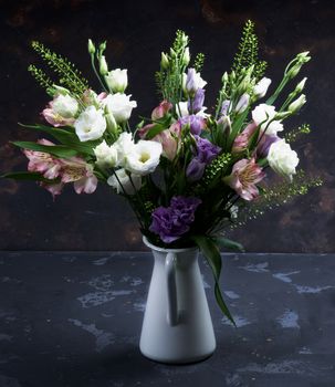 Elegant Flowers Bouquet with White and Purple Lisianthus, Alstroemeria and Decorative Green Stems in White Tin Jug closeup on Dark Grunge background