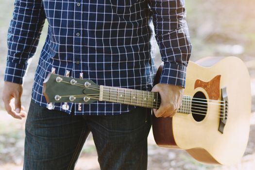Closeup photo of young man stand hold guitar in parks.
