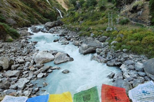 Rapids and waterfall in the narrow place of the mountain river in the Himalayas with Buddhist flags