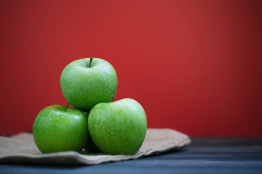 Group of green apples with fresh on a sack in a wooden desk and Red background.