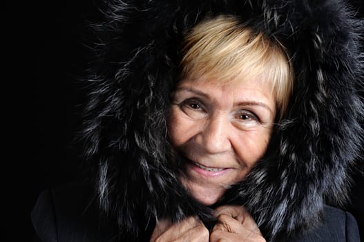 Portrait of a laughing middle-aged woman wrapped in a fur hood on a dark background close-up