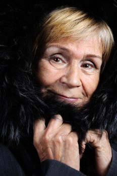 Portrait of an elderly woman wrapped in a fur hood on a dark background close-up