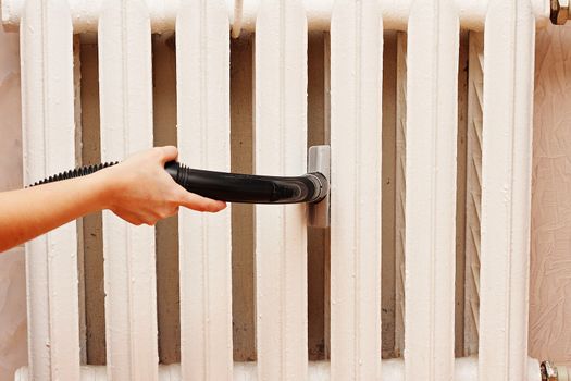 Woman vacuuming thoroughly cleans the radiator heating.