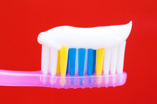 Squeeze a toothpaste on the toothbrush color pink in the red background.