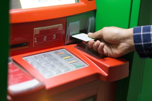 Hand inserting ATM card into bank machine to withdraw money