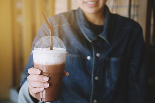 A young in a denim jacket Hold a chocolate drink cool in glass plastic Concept.