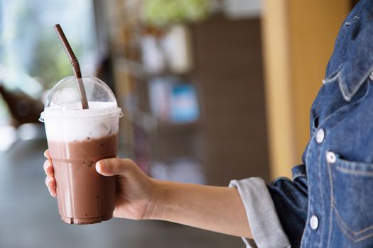 A young in a denim jacket Hold a chocolate drink cool in glass plastic Concept.