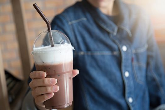 A young woman in a denim jacket Hold a chocolate drink cool in glass plastic Concept.