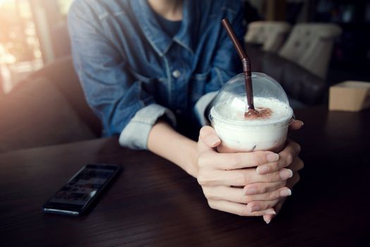 A young woman in a denim jacket a chocolate drink cool in glass plastic on wooden table Concept.