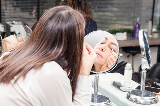 White woman removing makeup in front of mirror at beauty salon