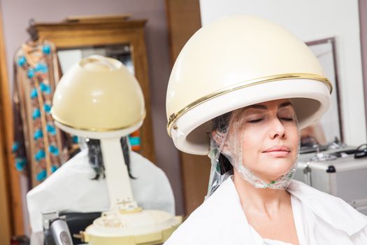 Woman under a professional hair steamer with a hair treatment