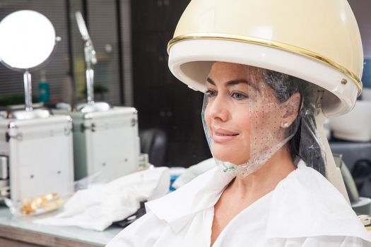 Woman under a professional hair steamer with a hair treatment