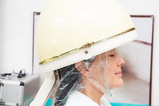 Woman under a professional hair steamer with a hair treatment