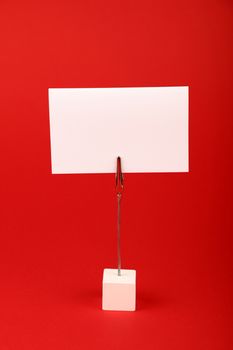 Blank white cardboard sign with copy space on metal note holder over red paper background, front side view