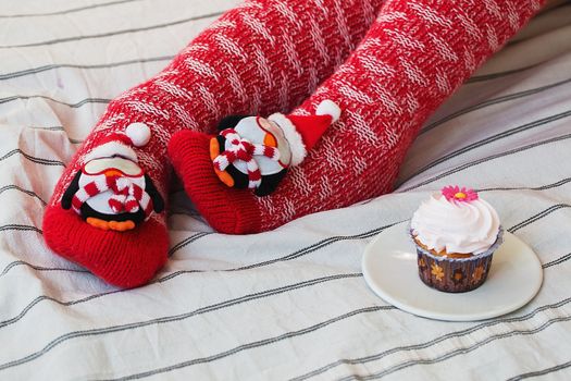 Cozy Christmas at home. Women's feet in Christmas stockings, big present, cup of tea, candy and Cookies Chocolate on bokeh light background. Top view. Selective focus. Toning.