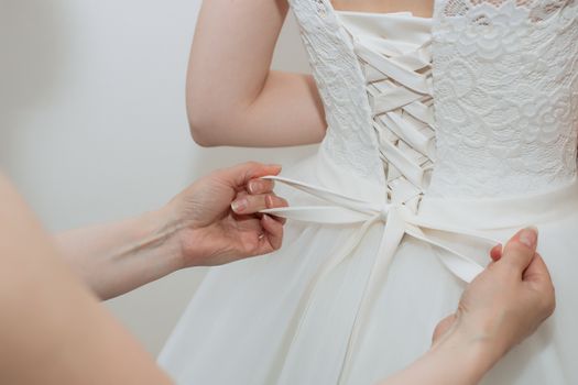 Mom helps daughter to wear wedding dress.