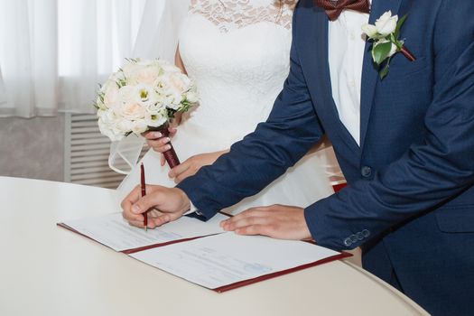 Young couple signing wedding documents. Focus on hand.