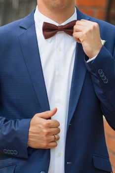 Stylish groom straightens a tie . Closeup of the clothed in blue jacket and white shirt at the park on their wedding day