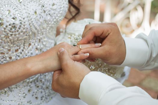 Wedding day. The groom places the ring on the bride's hand.