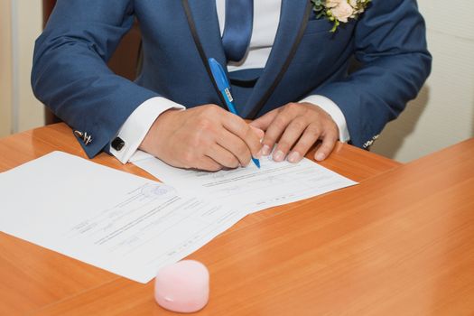 Young couple signing wedding documents. Focus on hand.