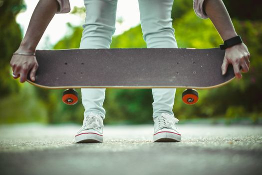 girl in white sneakers, holding a skateboard in hand close up