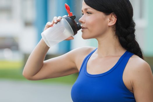 Fitness beautiful woman drinking water and sweating after exercising on summer hot day in beach. Female athlete after work out.