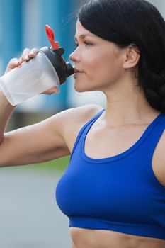 Fitness beautiful woman drinking water and sweating after exercising on summer hot day in beach. Female athlete after work out.