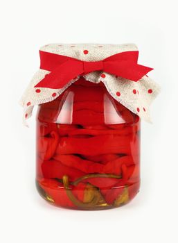 Close up of one glass jar of pickled red hot cherry chili pepperoncini peppers with linen canvas lid decoration and red ribbon over white background, low angle side view