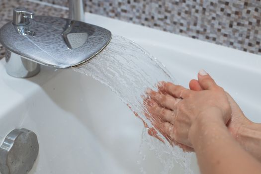 Washing of hands with soap under running water.