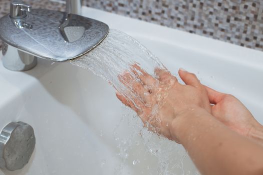 Washing of hands with soap under running water.