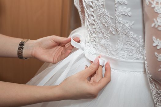 Mom helps daughter to wear wedding dress.