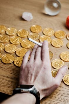 Man hand with a joint near bitcoin gold coins on the table.