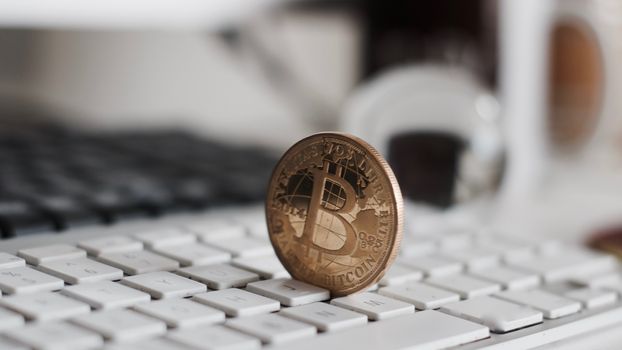 Digital currency physical metal bitcoin coin on the white keyboard near glass ball.