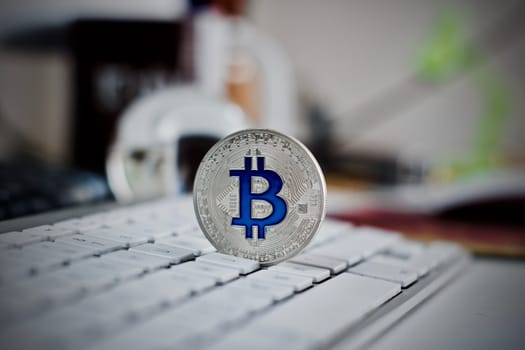Digital currency physical metal bitcoin coin on the white keyboard near glass ball.