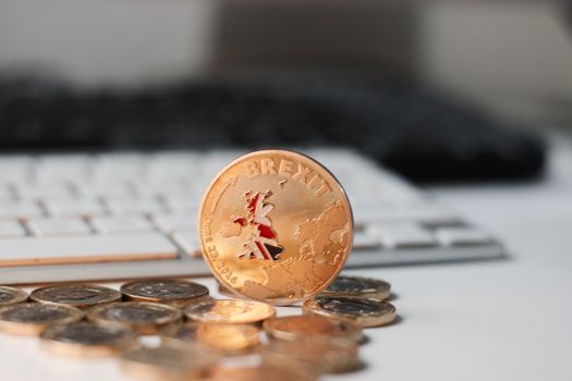 Europe leaving. Gold brexit coin with British map near keyboard and pound sterling.