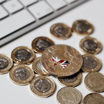 Europe leaving. Gold brexit coin with British map near keyboard and pound sterling.
