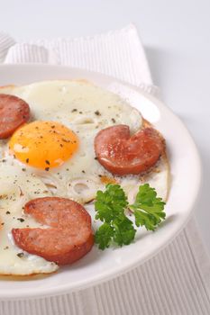fried eggs with sliced sausage on white plate