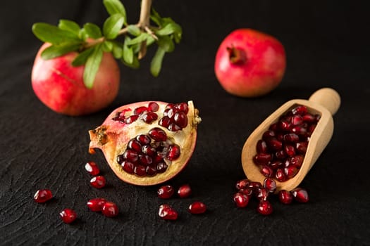 Ripe pomegranate fruits and bailer with seeds inside over a black textured background