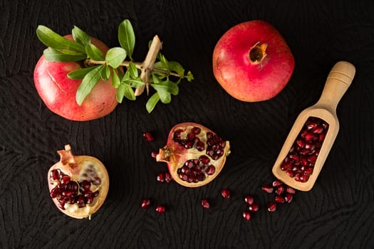 Ripe pomegranate fruits and bailer with seeds inside seen from above over a black textured background