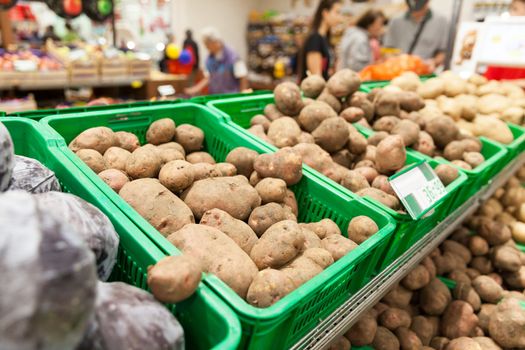 Potatoes on supermarket vegetable shelf, blurred buyers in the background