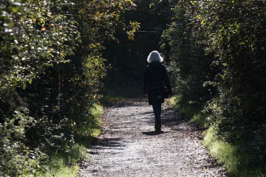 A senior blonde woman walks alone on a countryside pathway