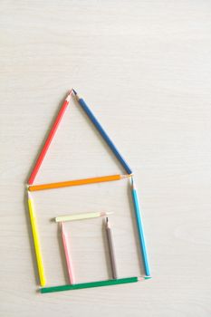 Crayons arranged as a symbol of the house on a wooden floor, house concept